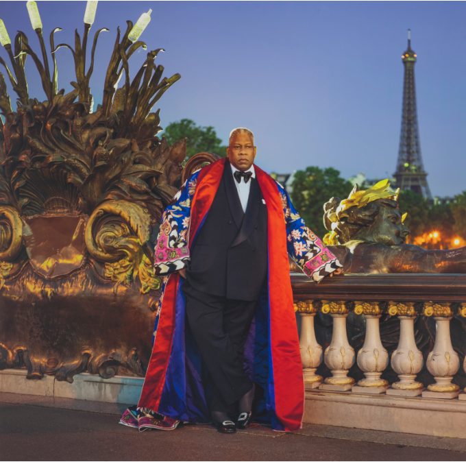 Man in a tuxedo and long colorful cape on a Paris bridge, Eiffel Tower behind him